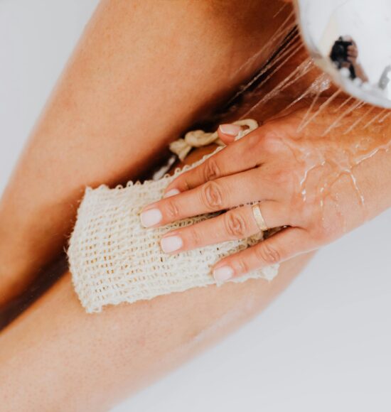 Close-up of a person exfoliating legs in the shower with a body scrubber.